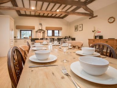 A dining table set with white bowls plates and glasses in a kitchen with wooden beams at Riven Oak in Lyth Valley near Levens