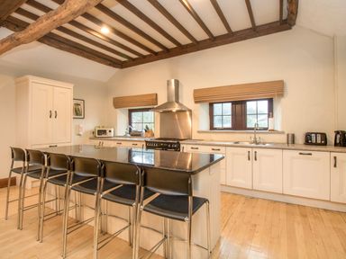 A kitchen with an island and bar stools under exposed wooden beams at Riven Oak in Lyth Valley near Levens