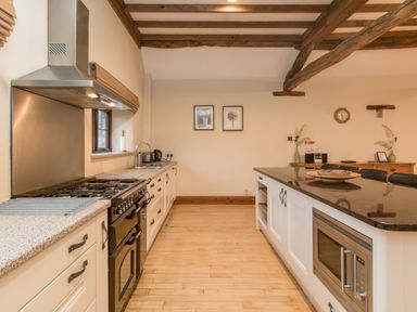 A kitchen with a stove, sink, microwave, and an island with chairs at Riven Oak in Lyth Valley near Levens