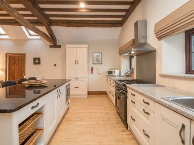 A kitchen with wooden ceiling beams a central island with chairs and kitchen appliances at Riven Oak in Lyth Valley near Levens