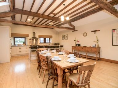 A dining area with a wooden table and chairs set with white dishes next to a kitchen with cabinets and a stainless steel range hood at Riven Oak in Lyth Valley near Levens