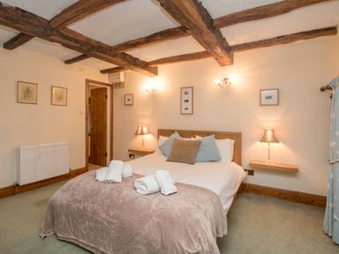 A bedroom with a double bed bedside lamps wooden ceiling beams and folded towels on the bed at Riven Oak in Lyth Valley near Levens