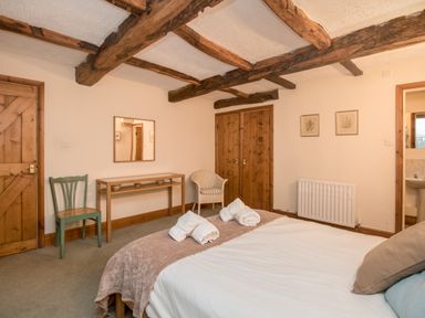 A bedroom with a bed folded towels wooden doors chairs and wooden ceiling beams at Riven Oak in Lyth Valley near Levens