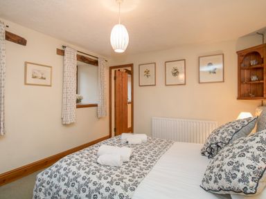 A bedroom with a bed with patterned pillows and folded towels on it framed floral artwork on the wall and wooden shelves at Riven Oak in Lyth Valley near Levens