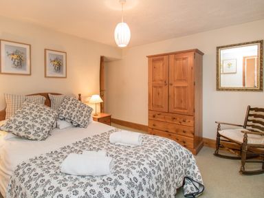 A bedroom with a double bed with patterned bedding bedside tables a wardrobe a rocking chair and framed pictures on the walls at Riven Oak in Lyth Valley near Levens