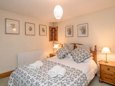 A bedroom with a double bed bedside tables lamps and framed botanical prints on the walls at Riven Oak in Lyth Valley near Levens
