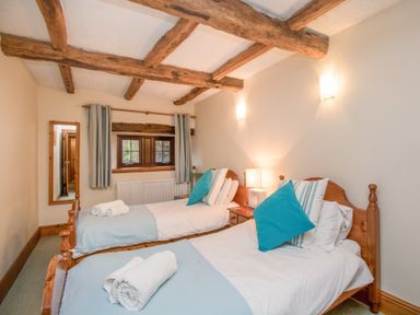 A bedroom with two single beds wooden beams on ceiling and a window with curtains at Riven Oak in Lyth Valley near Levens