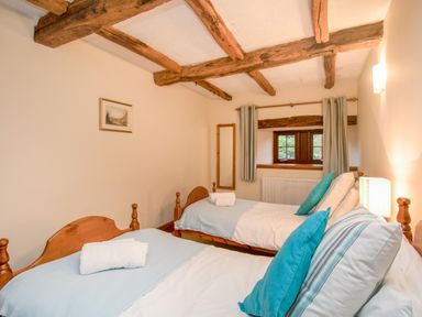 A bedroom with two single beds wooden beams on ceiling and a small window at Riven Oak in Lyth Valley near Levens
