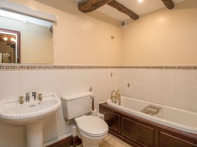 A bathroom with a pedestal sink, toilet, and bathtub with wood paneling at Riven Oak in Lyth Valley near Levens