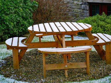 A wooden picnic table with attached benches covered with light snow in a garden at Riven Oak in Lyth Valley near Levens