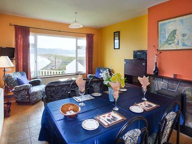 A dining room with a table set for four next to a seating area with armchairs and a window with a view at Rossbeigh Beach Cottage No 6 Rossbeigh near Glenbeigh County Kerry