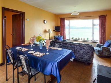 A dining area with a table set with plates and glasses next to a living room with sofas and a window view at Rossbeigh Beach Cottage No 6 Rossbeigh near Glenbeigh County Kerry