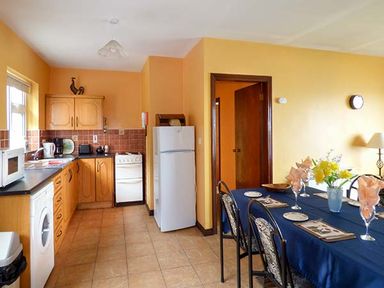 A kitchen and dining area with wooden cabinets white appliances and a dining table with blue tablecloth at Rossbeigh Beach Cottage No 6 Rossbeigh near Glenbeigh County Kerry