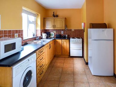 A kitchen with wooden cabinets white appliances and a brown tiled floor at Rossbeigh Beach Cottage No 6 Rossbeigh near Glenbeigh County Kerry