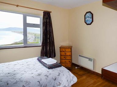 A bedroom with a bed a window with a curtain and a wooden chest of drawers at Rossbeigh Beach Cottage No 6 Rossbeigh near Glenbeigh County Kerry