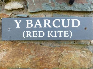 A sign on a stone wall with the text Y Barcud Red Kite at Y Barcud in Holyhead