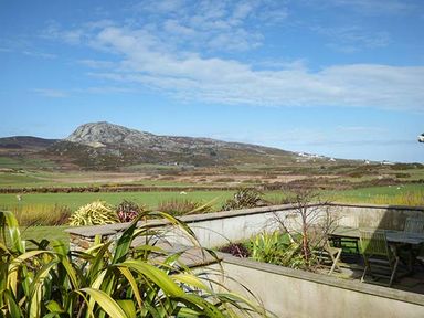 An outdoor patio area with table and chairs surrounded by plants with hills and fields in the background at Y Barcud in Holyhead