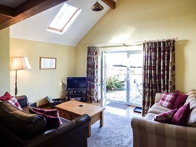 A living room with two sofas a wooden coffee table a floor lamp and a TV near glass doors at Y Barcud in Holyhead