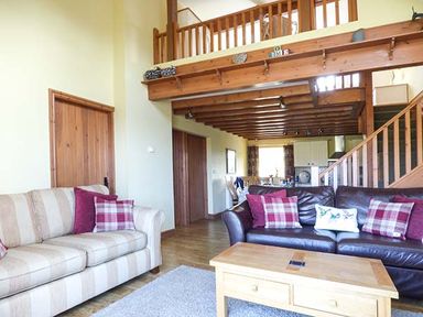 A living room with two sofas and a wooden coffee table under a wooden balcony at Y Barcud in Holyhead