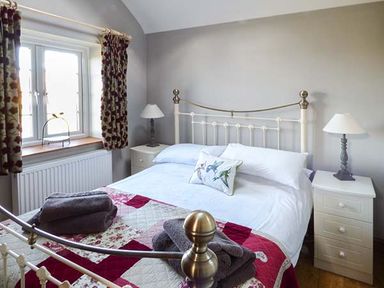A bedroom with a metal bed frame bedside tables lamps and folded towels on the bed at Y Barcud in Holyhead
