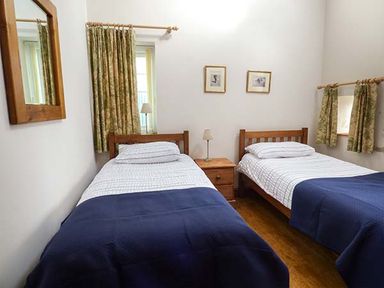 A bedroom with two single beds a nightstand and windows with curtains at Y Barcud in Holyhead
