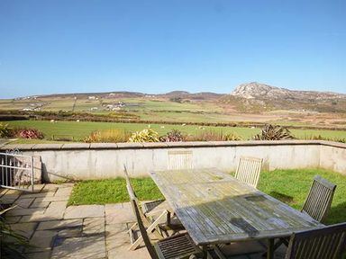 An outdoor patio with a wooden table and chairs overlooking fields and hills at Y Barcud in Holyhead
