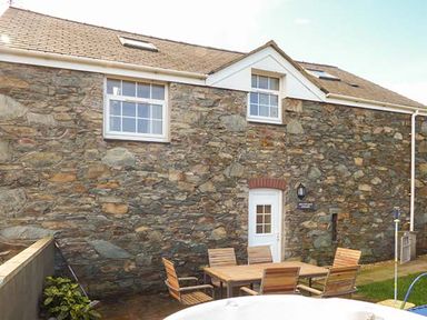 A stone exterior wall of a building with a white door and windows and wooden chairs around a wooden table at Bran Goesgoch in Holyhead