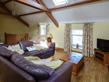 A living room with brown leather sofas wooden coffee table television and floral curtains at Bran Goesgoch in Holyhead