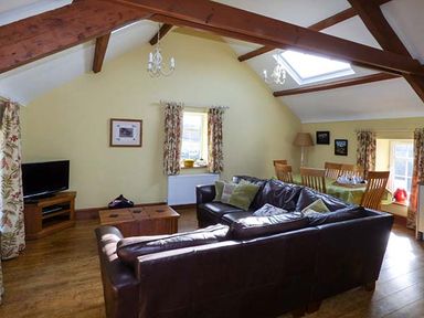 A living room with a brown leather sofa a wooden coffee table a television on a wooden stand and a dining table with chairs at Bran Goesgoch in Holyhead