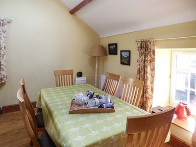 A dining room with wooden chairs around a table with a tray of tea items and a window with curtains at Bran Goesgoch in Holyhead