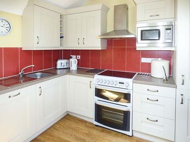 A kitchen with white cabinets a stove a microwave a toaster a kettle and a sink at Bran Goesgoch in Holyhead
