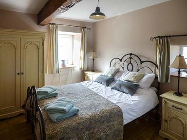 A bedroom with a double bed with pillows and folded towels bedside tables with lamps a wardrobe and curtains at Bran Goesgoch in Holyhead