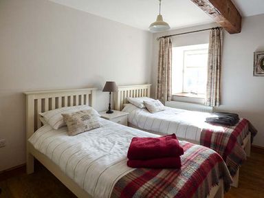 A bedroom with two single beds a bedside table with a lamp and a window with curtains at Bran Goesgoch in Holyhead