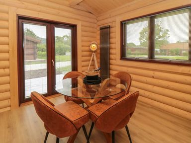 A dining area with a glass table and four brown chairs near windows and wooden walls at Carlton Lodge 1 in Stokesley
