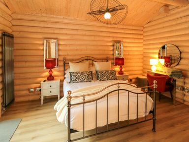 A bedroom with a metal bed frame bedside tables with red lamps and a dressing table with a round mirror and red chair at Carlton Lodge 1 in Stokesley
