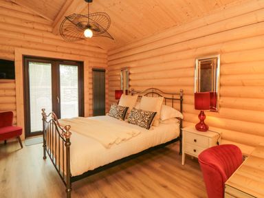 A bedroom with a metal bed frame two bedside tables with lamps a red chair and wooden walls and floor at Carlton Lodge 1 in Stokesley
