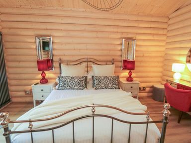 A bedroom with a metal bed frame two bedside tables with red lamps two mirrors and a red chair at Carlton Lodge 1 in Stokesley