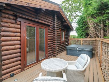 An outdoor wooden deck with wicker chairs a round table a hot tub and a log cabin exterior in Stokesley
