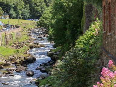 A rocky stream with flowing water beside a stone building and a road with parked cars and trees at Clooneavin Apartment 3 in Lynmouth near Lynton