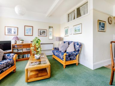 A living room with two blue floral armchairs a wooden coffee table with a plant and a sideboard with books and decorations at Clooneavin Apartment 3 Lynmouth near Lynton