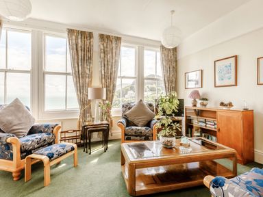 A living room with armchairs a coffee table plants and large windows overlooking the sea at Clooneavin Apartment 3 Lynmouth near Lynton