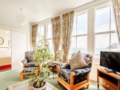 A living room with patterned armchairs a plant and a television at Clooneavin Apartment 3 in Lynmouth near Lynton