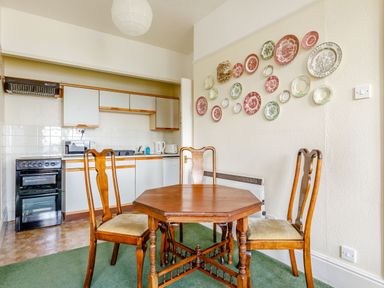 A kitchen with white cabinets a black stove a wooden table with three chairs and decorative plates on the wall at Clooneavin Apartment 3 in Lynmouth near Lynton