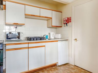 A kitchen with white cabinets wooden handles a microwave kettle toaster and sink next to a white door at Clooneavin Apartment 3 in Lynmouth near Lynton