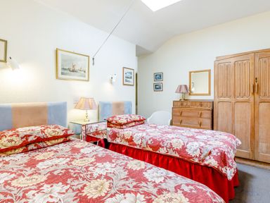 A bedroom with two single beds with floral bedspreads a wooden wardrobe a wooden dresser with a lamp a white chair and paintings on the walls at Clooneavin Apartment 3 in Lynmouth near Lynton