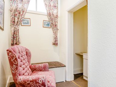 A small room with a pink upholstered armchair floral curtains and a small storage bench at Clooneavin Apartment 3 Lynmouth near Lynton