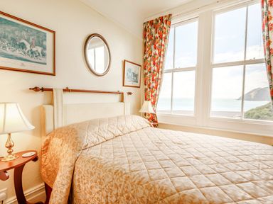 A bedroom with a bed two bedside tables with lamps framed pictures and a window with floral curtains at Clooneavin Apartment 3 Lynmouth near Lynton
