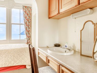 A bedroom with a bed near a window with floral curtains and a countertop with a sink and mirror at Clooneavin Apartment 3 in Lynmouth near Lynton