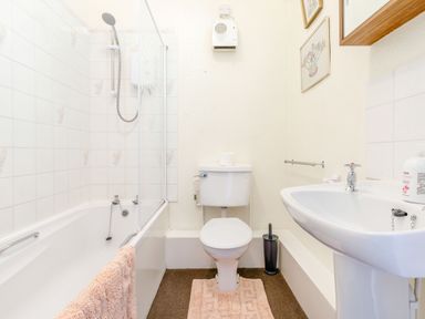 A bathroom with a bathtub and shower, toilet, sink, and a pink bath mat at Clooneavin Apartment 3 Lynmouth near Lynton