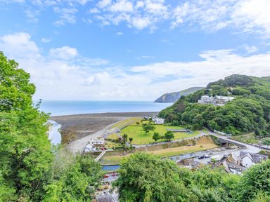 A coastal landscape with trees a rocky beach buildings and a large green field at Clooneavin Apartment 3 in Lynmouth near Lynton
